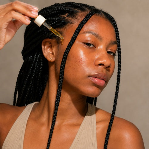 Woman applying oil to her braided hair with a dropper.