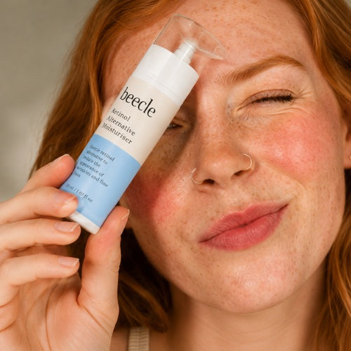 Woman holding a bottle of 'beeacle' retinol alternative moisturizer close to her face.